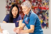 Zwei Frauen unterschiedlichen Alters betrachten gemeinsam ein Tablet für digitale Unterstützung und Zusammenarbeit im rotkreuzCRM.