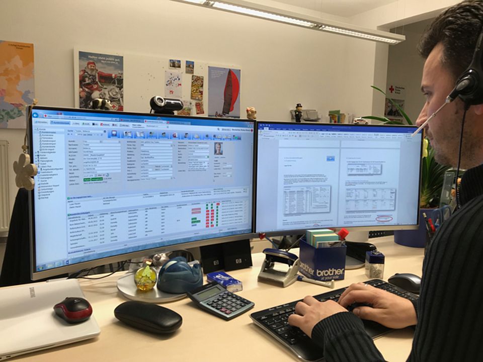 Dieses Imagebild für Kontaktangaben zeigt einen DRK-Mitarbeiter, der an einem Doppelmonitor mit dem rotkreuzCRM arbeitet.